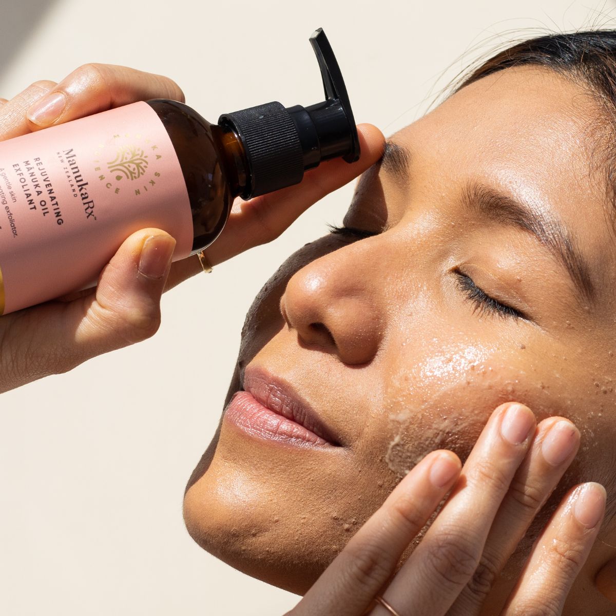 Woman holding bottle of Rejuvenating Manuka Oil Exfoliant while applying the product to her face